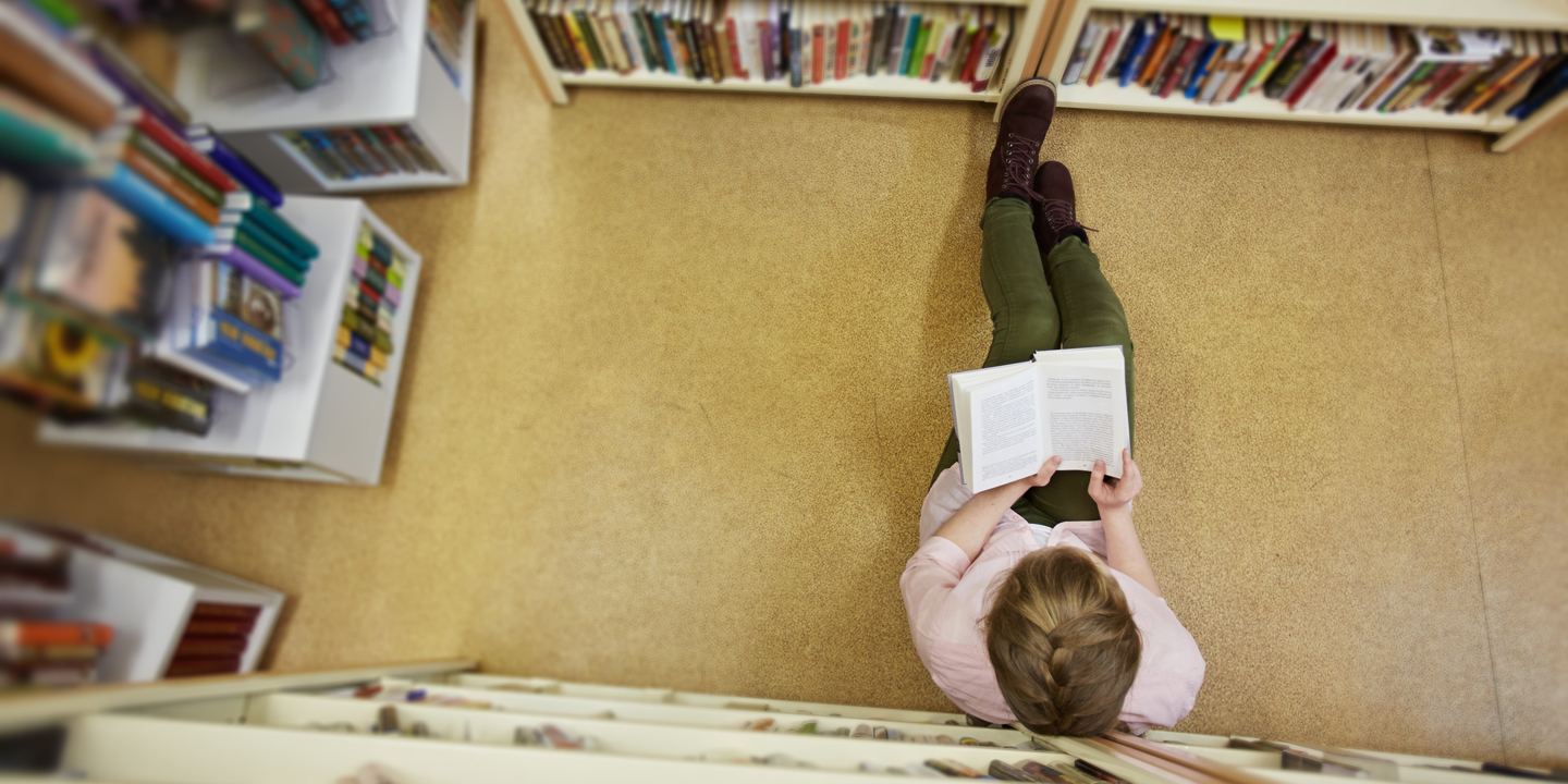 Jugendliche sitzt am Boden in einer Bibliothek und liest ein Buch