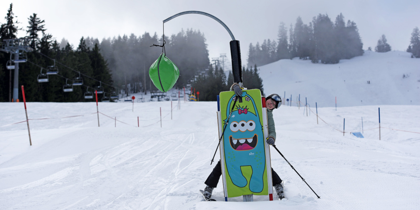 Eine Jugendliche ist auf der Skipiste und umararmt ein Hindernis von einem Kinderparcours, dass wie ein Monster aussieht.
