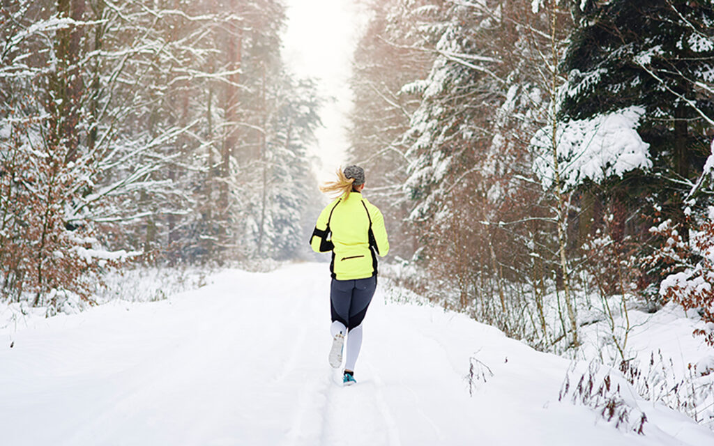 Junge Frau joggt einen verschneiten Weg entlang