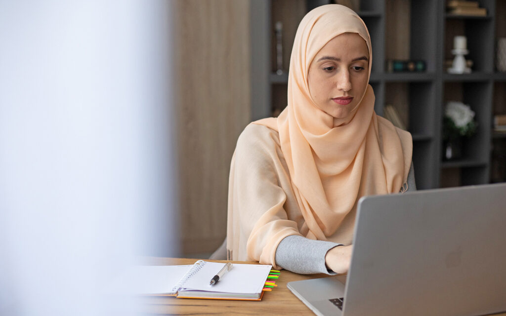 Junge Frau mit Kopftuch sucht am Computer nach einer Lehrstelle