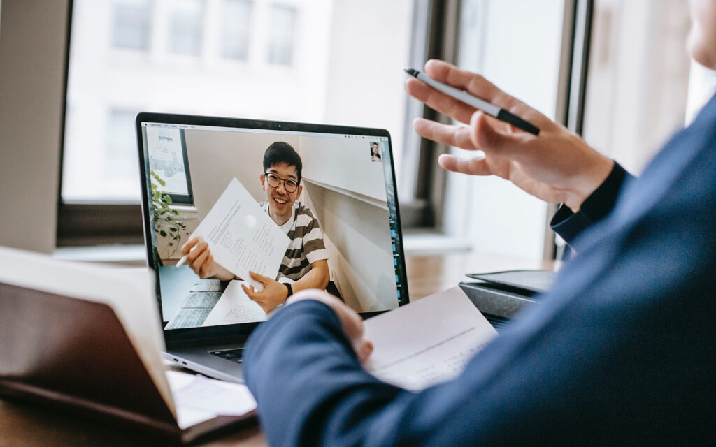 Ein Mann f&uuml;hrt mit einem jungen Mann ein Bewerbungsgespr&auml;ch online &uuml;ber den Computer