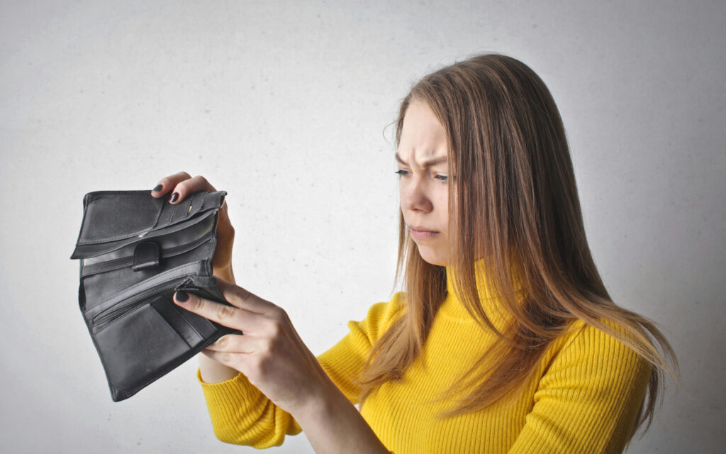 Eine junge Frau schaut ver&auml;rgert in ihre leere Geldtasche.