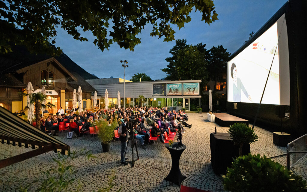 Zuschauer*innen schauen sich drau&szlig;en unter freiem Himmel einen Film auf Kinoleinwand an