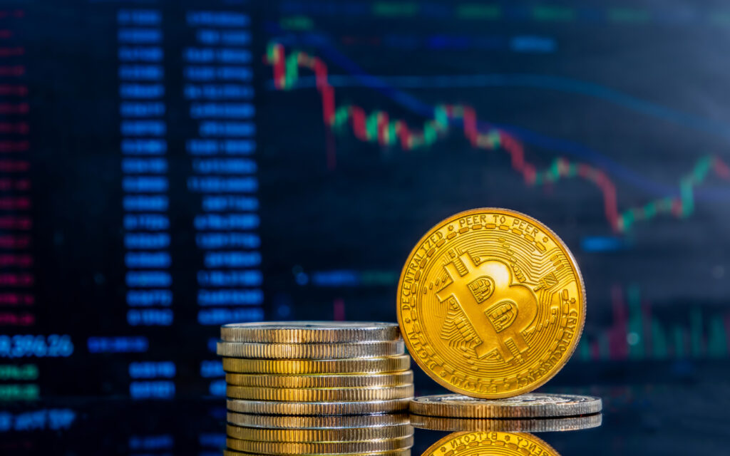 Nahaufnahme von goldenen Bitcoins auf einer dunklen, reflektierenden Oberfl&auml;che und dem Histogramm der abnehmenden Kryptow&auml;hrung im Hintergrund.