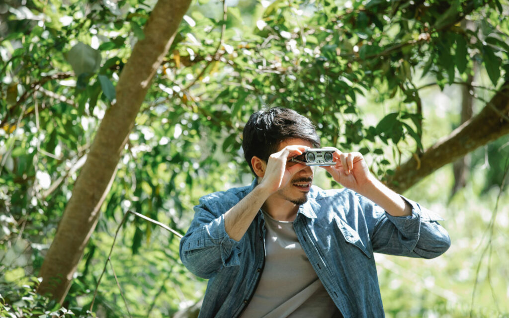 Ein junge Mann in der Natur mit einem Fernglas.