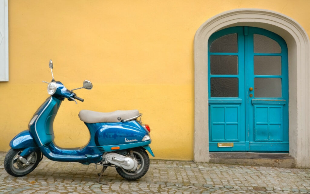 Eine Vespa steht vor einer gelben Wand.