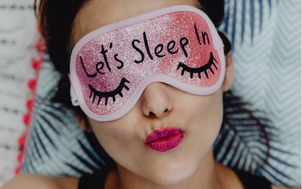 Eine Frau mit Schlafmaske auf der steht "Let's Sleep In".