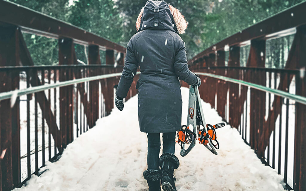 Junge Frau geht mit Schneeschuhen &uuml;ber eine verschneite Br&uuml;cke
