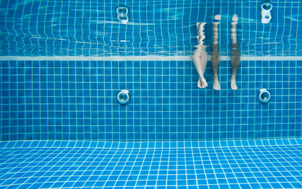 Zwei Paar Füße, die in einem blauen Schwimmbecken baumeln.