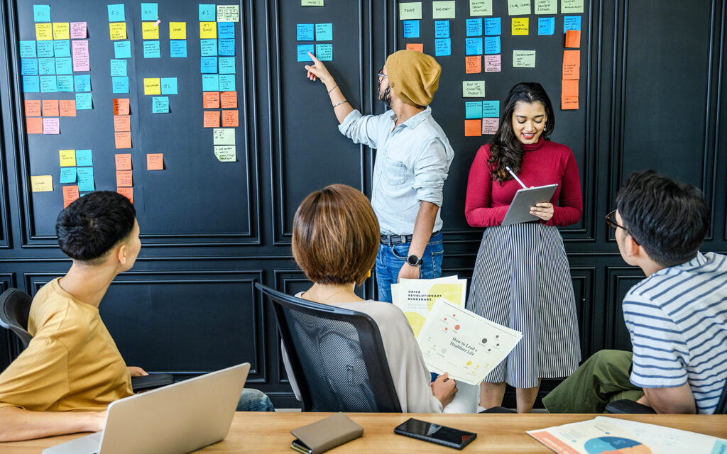 Eine Gruppe macht Brainstorming und schreibt die Ideen auf Post its, die sie an die Wand h&auml;ngen