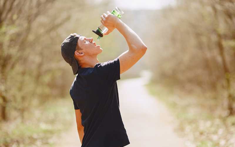 Ein junger Mann trinkt aus einer Flasche im Sommer.